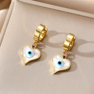 Detail of gold heart earrings with white shell inlay and blue evil eye charms