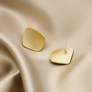 Matte gold geometric trapezoid earrings with brushed metal finish on silk background