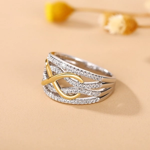 Macro shot of silver wide band ring with gold infinity knot and pavé set zircons
