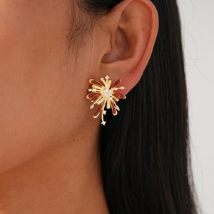 Close-up of golden starburst earrings with red enamel and heart-shaped center on model
