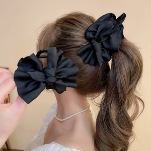 Detail of a large matte black fabric bow hair claw clip styled on a low ponytail