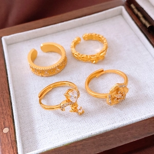 Detail of four vintage 24K gold plated rings with floral and zircon designs in a wooden box