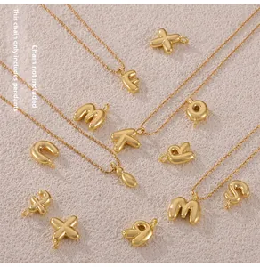 Detailed close-up of gold-plated balloon letter pendants on a textured pink surface