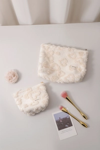 Flat lay of cream plush cosmetic bags with H&R logo, makeup brushes and white flowers