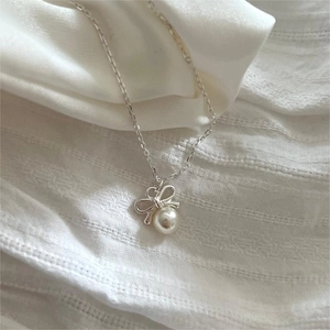 Detail of silver bow pendant with white pearl on minimalist chain and soft fabric
