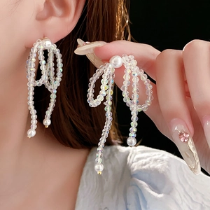Detail of crystal bow earrings with dangling fringe and pearls worn by a model