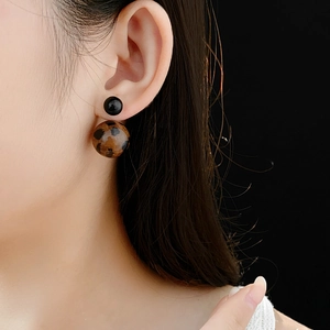 Close-up of leopard print double bead stud earrings worn by a model on black background