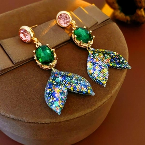 Détail de boucles d'oreilles queue de sirène avec paillettes et pierres vertes ovales