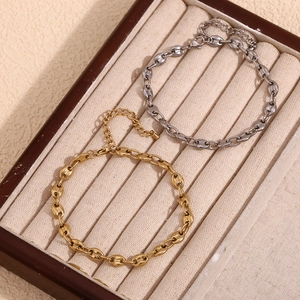 Detail of coffee bean link bracelets in gold and silver finish on beige velvet tray