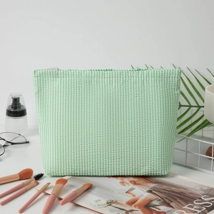 Detailed view of green seersucker striped makeup bag with zipper on a white desk setup