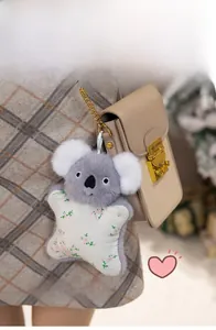 Plush koala charm with floral star embroidery attached to a khaki chain handbag