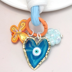 Détail de porte-clés œil maléfique avec cœur bleu, papillon orange et charms de fleurs
