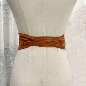 Detail of brown leather wide waist belt with crisscross design on a white mannequin