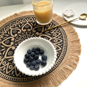 Round woven jute placemat with black mandala pattern and fringe tassels for dining decor