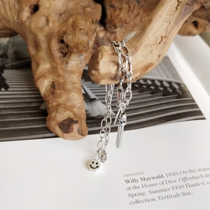 Elegant S925 sterling silver bracelet featuring a smile charm and metal tassel on wood