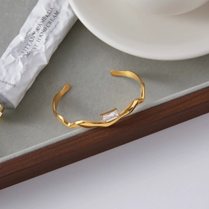 Detail shot of a wavy 18K gold-plated stainless steel bracelet with square zircon