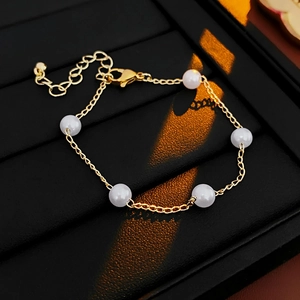 Detailed close-up of a gold minimalist pearl bracelet on a textured black jewelry box