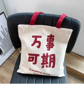 Detailed view of a white canvas tote bag with red handles and text on a black chair