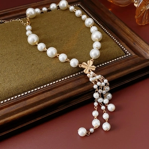 Macro detail of artificial pearl flower necklace with tassels and gold four-leaf clover