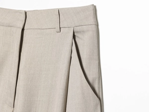 Detail showing high-waist pleats and pocket stitching on beige tailored trousers