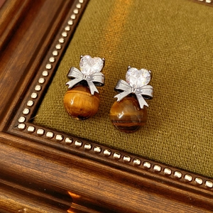Close-up of heart zircon bow earrings with brown tiger eye stone on green fabric
