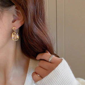 Detail of geometric gold earrings with clear crystals and a carved silver band ring