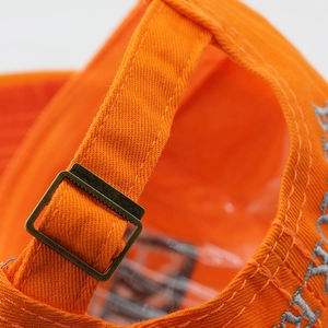 Detail of the vintage bronze buckle and adjustable cotton strap on a vibrant orange baseball cap
