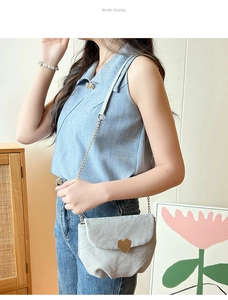 Détail d'un sac selle plissé gris avec un fermoir cœur doré et une bandoulière chaîne