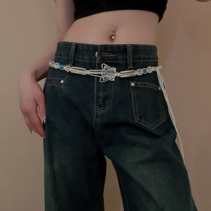 Detail of bohemian waist chain with silver butterfly pendant and woven blue beads on denim