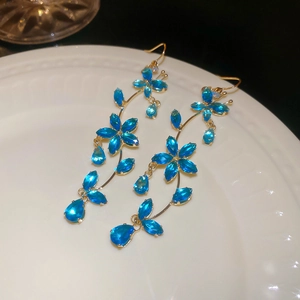 Macro detail of gold floral dangle earrings featuring sparkling blue crystal marquise petals