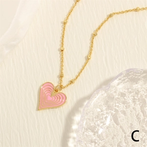 Macro shot of gold beaded chain featuring a layered pink enamel heart pendant