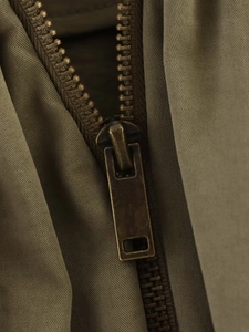 Macro view of vintage bronze zipper detail on olive green quilted jacket fabric
