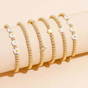 Detail of gold beaded bracelets with MAMA letters and heart charms on a display stand