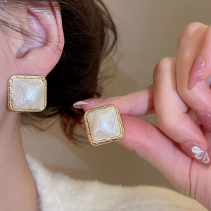 Close-up of gold-plated square mother of pearl stud earrings worn by a model