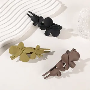 Three matte butterfly hair clips in black, olive, and brown colors on a white display stand