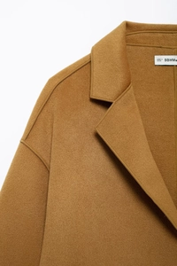 Detailed close-up of the lapel and shoulder stitching on a caramel wool coat
