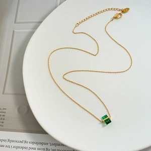Elegant gold necklace featuring a green rhombus crystal pendant on a white ceramic plate