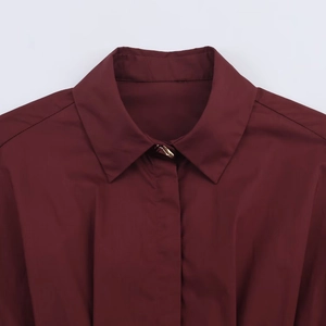 Detail of burgundy poplin shirt featuring a classic lapel and single gold metal button
