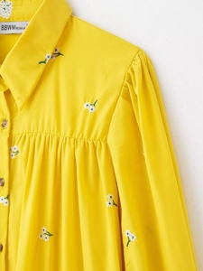 Detailed close-up of yellow cotton shirt featuring white floral embroidery and puff sleeves