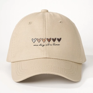 Detail of khaki cotton baseball cap featuring heart icons and one day at a time text