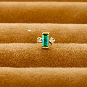 Macro shot of an emerald-cut green stone earring with white zircons in a gold setting