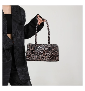 Detail of leopard print baguette bag with heart pendant held by a model in a black suit