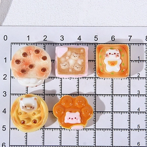 Close-up of 2-3cm resin cat-themed charms and miniature cat paw dessert on measuring mat