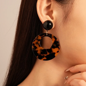 Close-up of a model wearing large leopard print resin hoop earrings with retro black beads