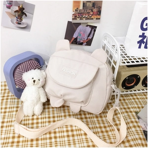 Close-up of cute cream canvas crossbody bag with teddy bear charm and fashion logo