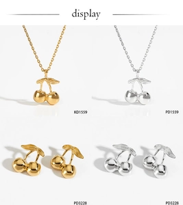 Detailed close-up of cherry pendant necklace and earrings set in gold and silver finishes