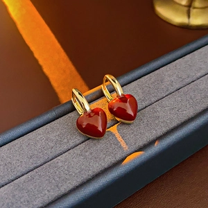 Detail of gold-plated red enamel heart earrings on a warm display box background