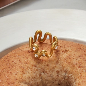 Détail d'une bague dorée ondulée ornée de zircons posée sur un bagel artisanal