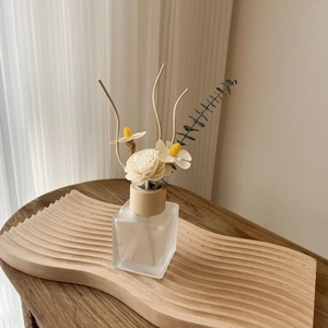 Reed diffuser with dried flowers in frosted glass on a wooden tray for home decor