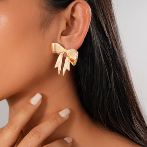 Close-up of a model wearing a large golden metallic bow-knot earring with a glossy finish